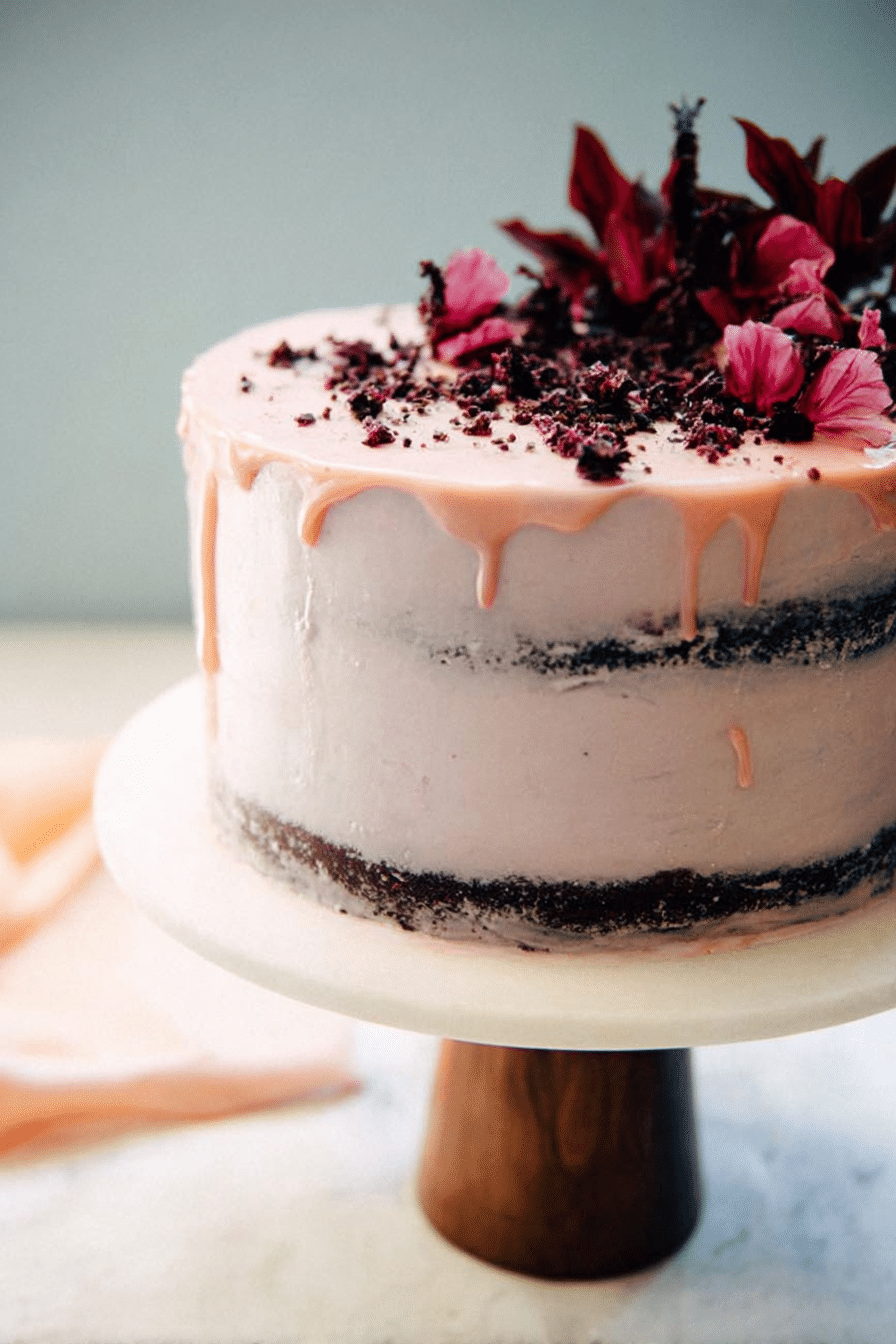 Naked hibiscus chocolate cake with layers of chocolate and hibiscus frosting, garnished with fresh hibiscus flowers.