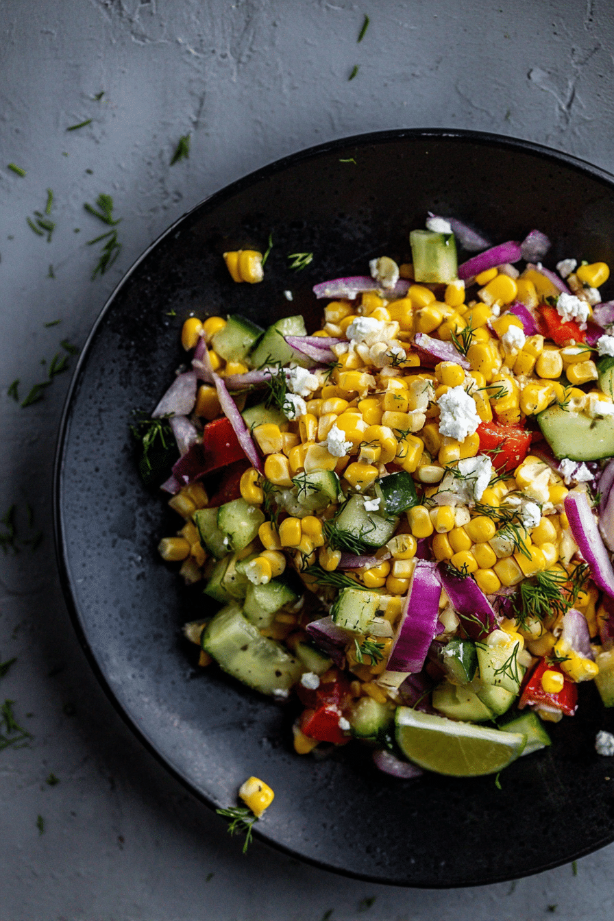 Bright and colorful refreshing corn salad with lime dressing and feta cheese on a wooden table